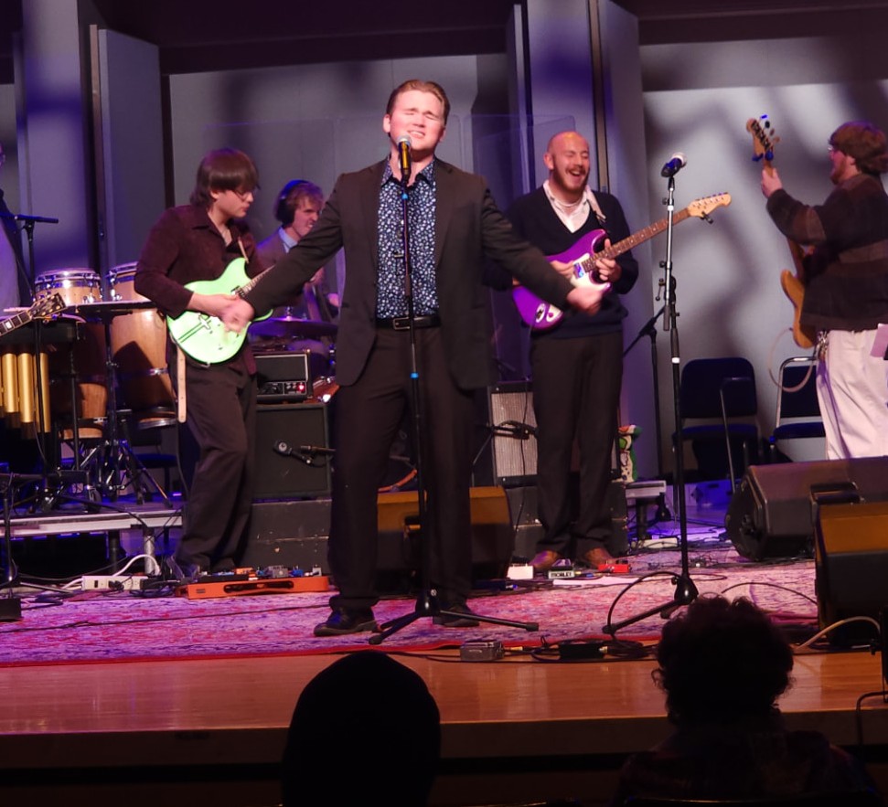 Corwin Belnap singing with his band on an auditorium stage