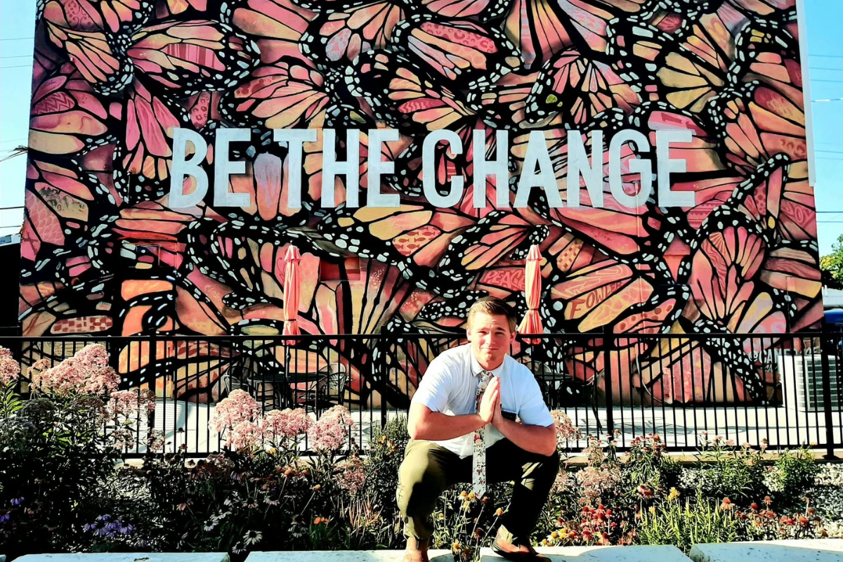 Corwin as a missionary, kneeling in front of a Be the Change butterfly mural